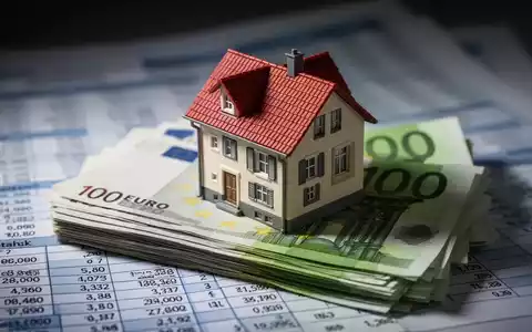 Ein detailliertes Miniaturhausmodell steht auf einem Stapel deutscher Euro-Banknoten, im Hintergrund verschwommene Finanzdokumente. - Foto: über boerse-global.de