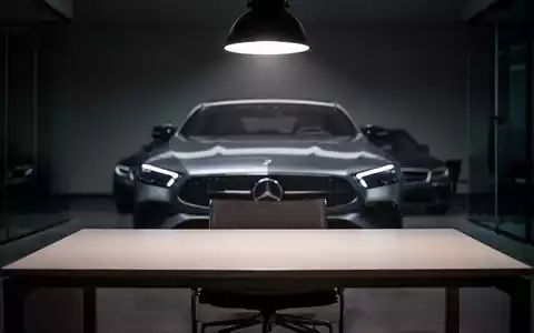 Ein unscharfer Mercedes-Benz im Hintergrund, im Vordergrund ein leerer Büroschreibtisch unter grellem Licht. Symbolisiert das Ende des Homeoffice. - Foto: über boerse-global.de