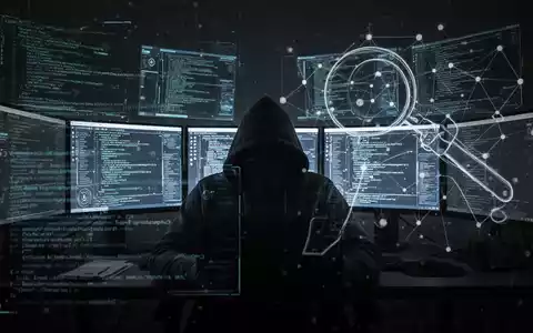 Eine Schattenfigur in einem dunklen Raum, erleuchtet von mehreren Bildschirmen mit Code und digitalen Schnittstellen, symbolisiert Cyberkriminalität und Überwachung. - Foto: über boerse-global.de