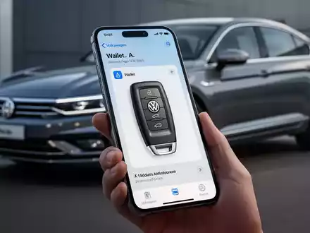 Ein iPhone zeigt die Apple Wallet Autoschlüssel-Oberfläche für einen Volkswagen, im Hintergrund ein Auto. - Foto: über boerse-global.de