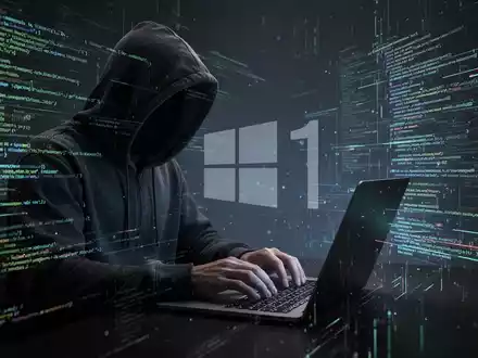 Verschwommene Gestalt in Kapuzenjacke tippt auf Laptop, umgeben von leuchtenden Codezeilen und Datenströmen, symbolisiert Cyberkriminalität und Ermittlung. - Foto: über boerse-global.de
