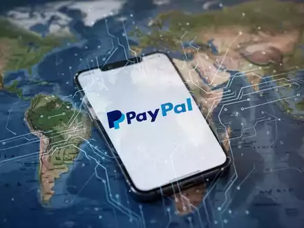 Ein Smartphone mit PayPal-Logo, digitale Linien verbinden sich mit einer unscharfen Karte von Asien und Ostafrika im Hintergrund. - Foto: über boerse-global.de