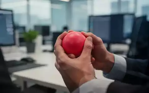 Hände halten einen Stressball in einem Büro, symbolisiert Stressprävention und Wohlbefinden am Arbeitsplatz. - Foto: über boerse-global.de
