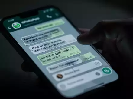 Nahaufnahme eines Smartphone-Bildschirms mit WhatsApp-Chat, unscharfe Hand greift danach, Symbol für digitalen Betrug. - Foto: über boerse-global.de