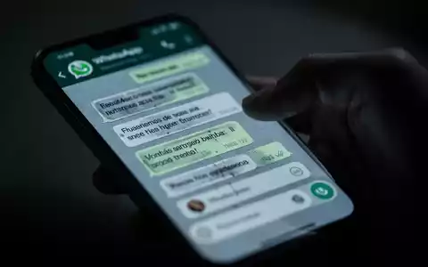 Nahaufnahme eines Smartphone-Bildschirms mit WhatsApp-Chat, unscharfe Hand greift danach, Symbol für digitalen Betrug. - Foto: über boerse-global.de