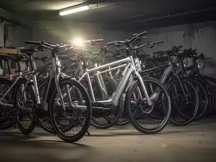 Mehrere hochwertige E-Bikes stehen dicht gedrängt in einem leicht schmutzigen Kellerraum, das Licht reflektiert auf den Rahmen. - Foto: über boerse-global.de