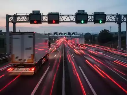 Eine Langzeitbelichtungsaufnahme von Lastwagen auf einer italienischen Autobahn bei Dämmerung, mit verschwommenen roten Rücklichtern. - Foto: über boerse-global.de