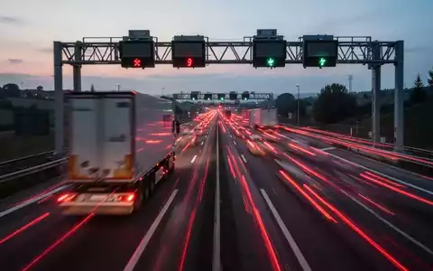 Eine Langzeitbelichtungsaufnahme von Lastwagen auf einer italienischen Autobahn bei Dämmerung, mit verschwommenen roten Rücklichtern. - Foto: über boerse-global.de