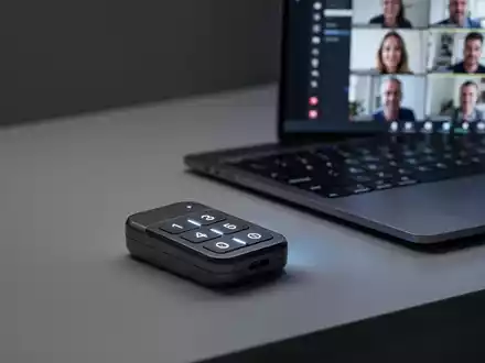Ein schlankes, modernes Mini-Keypad mit drei beleuchteten Tasten auf einem minimalistischen Schreibtisch neben einem Laptop mit einer Videokonferenz. - Foto: über boerse-global.de