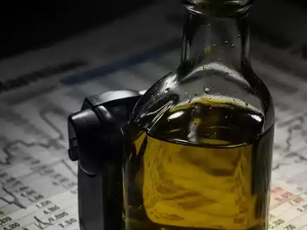 Nahaufnahme einer dunklen Olivenölflasche mit verschwommenem Hintergrund, der Finanzdokumente andeutet, symbolisiert Betrug in der Olivenölindustrie. - Foto: über boerse-global.de