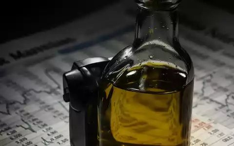 Nahaufnahme einer dunklen Olivenölflasche mit verschwommenem Hintergrund, der Finanzdokumente andeutet, symbolisiert Betrug in der Olivenölindustrie. - Foto: über boerse-global.de
