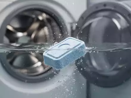 Eine Spülmaschinentablette löst sich in Wasser auf, im unscharfen Hintergrund ist die Trommel einer Waschmaschine zu sehen. - Foto: über boerse-global.de