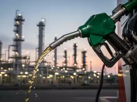 Eine Zapfpistole füllt einen Tank, im Hintergrund eine moderne Ölraffinerie bei Sonnenuntergang. Symbolisiert Tankrabatt-Untersuchung. - Foto: über boerse-global.de