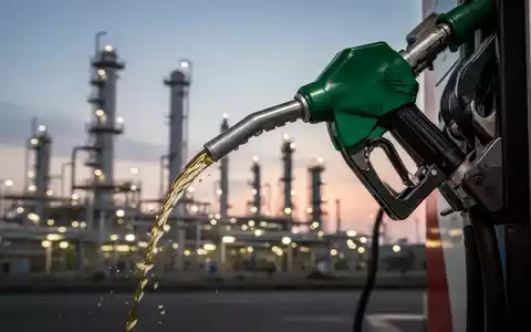 Eine Zapfpistole füllt einen Tank, im Hintergrund eine moderne Ölraffinerie bei Sonnenuntergang. Symbolisiert Tankrabatt-Untersuchung. - Foto: über boerse-global.de