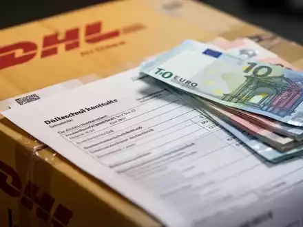 Ein verschwommenes DHL-Paket mit Fokus auf einem deutschen Steuerdokument oder Euro-Banknoten, das steuerliche Änderungen im Postsektor darstellt. - Foto: über boerse-global.de