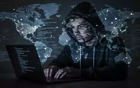 Schattenhafte Figur in Kapuzenpulli tippt auf Laptop, mit Code und Weltkarte als Projektionen, symbolisiert Cyber- und Georisiken. - Foto: über boerse-global.de