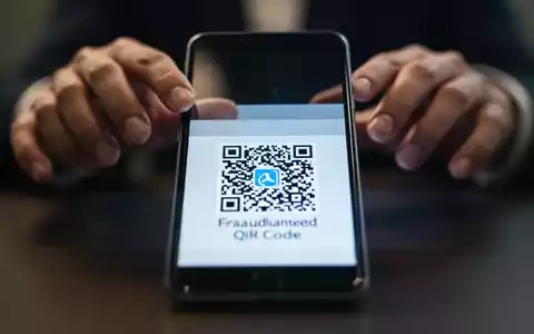 Ein Smartphone-Bildschirm zeigt einen betrügerischen QR-Code. Im Hintergrund sind unscharf Hände zu sehen, die zögern. - Foto: über boerse-global.de