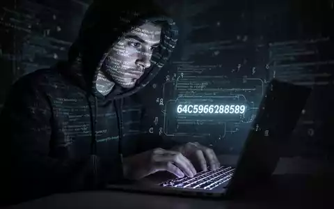 Eine Person im Kapuzenpulli tippt auf einer beleuchteten Tastatur, während Code und digitale Symbole auf ihr Gesicht projiziert werden. - Foto: über boerse-global.de