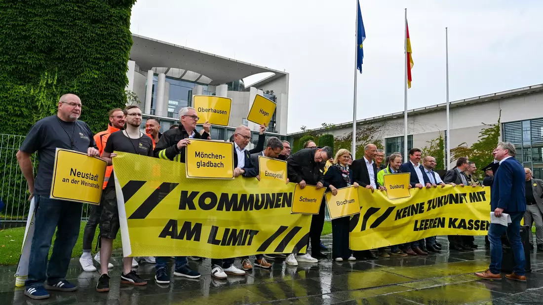 Vertreter mehrerer Städte und Kommunen demonstrieren mit Schildern und Bannern für finanzielle Unterstützung in Berlin. - Bild: Jens Kalaene/dpa