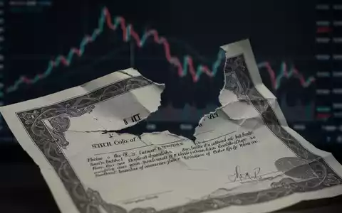 Eine teilweise zerrissene oder zerknüllte Aktienurkunde vor einem verschwommenen, fallenden Finanzindex-Chart. - Foto: über boerse-global.de