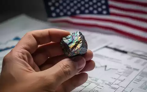 Nahaufnahme einer Hand, die ein seltenes Erdmineral hält, mit unscharfen Finanzdokumenten und US-Flagge im Hintergrund. - Foto: über boerse-global.de