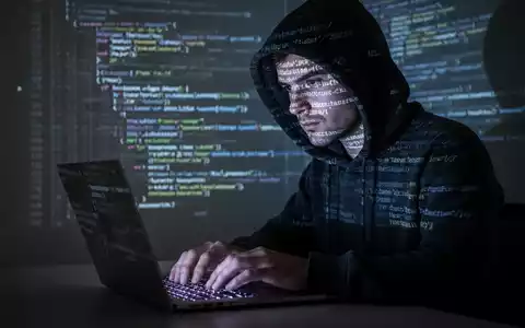 Eine Person mit Kapuze tippt auf einem Laptop, Code-Zeilen spiegeln sich im Gesicht und im Hintergrund wider, symbolisiert eine Datenpanne. - Foto: über boerse-global.de