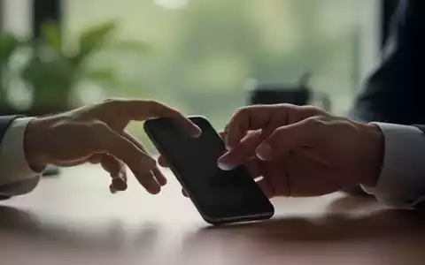 Eine Hand greift nach einem Smartphone, zögert aber, mit einem verschwommenen Hintergrund, der Ruhe oder einen Arbeitsplatz andeutet. - Foto: über boerse-global.de