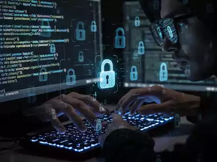Hackerhände tippen auf einer Tastatur, mit digitalen Sicherheitsschloss-Symbolen auf dem Bildschirm, der Code spiegelt sich in der Brille. - Foto: über boerse-global.de