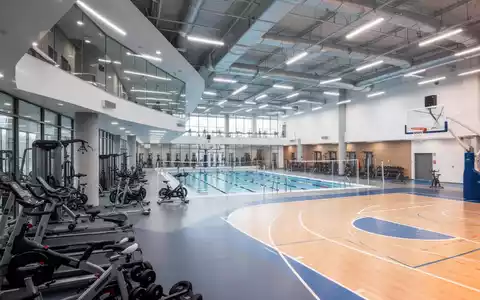 Innenansicht eines modernen Sportvereinszentrums mit Fitnessgeräten, Schwimmbecken und Sporthalle, symbolisiert Investitionen in Sportinfrastruktur. - Foto: über boerse-global.de