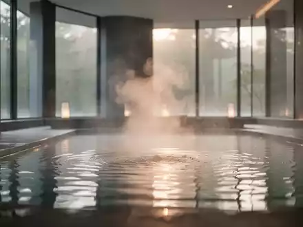 Ein ruhiges Thermalbad mit aufsteigendem Dampf, warmes Licht fällt durch große Fenster und schafft eine entspannende Atmosphäre. - Foto: über boerse-global.de
