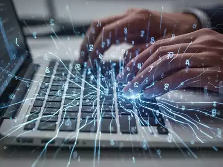 Nahaufnahme einer Laptop-Tastatur mit leuchtend blauen KI-Linien und Tabellenrastern, Hände bereit zum Tippen, symbolisiert KI-gesteuerte Produktivität. - Foto: über boerse-global.de