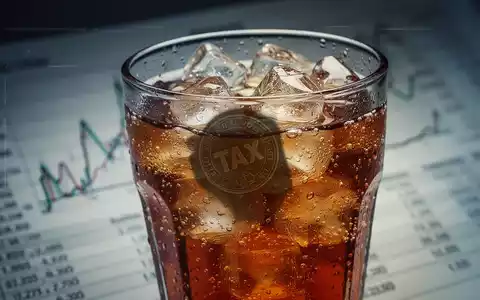 Ein Glas eines kohlensäurehaltigen Zuckergetränks mit Eiswürfeln. Der Schatten eines Münze oder Steuerstempels fällt auf das Glas. - Foto: über boerse-global.de