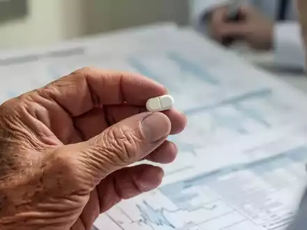 Nahaufnahme der Hand eines älteren Menschen, der eine kleine Pille hält, mit einem unscharfen medizinischen Hintergrund. - Foto: über boerse-global.de