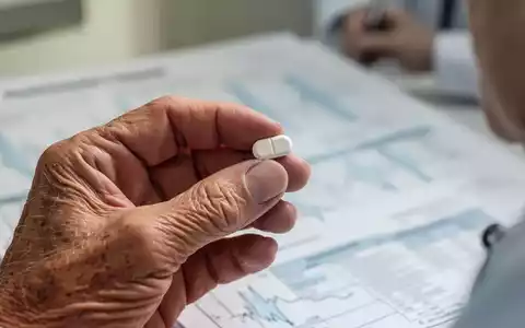 Nahaufnahme der Hand eines älteren Menschen, der eine kleine Pille hält, mit einem unscharfen medizinischen Hintergrund. - Foto: über boerse-global.de