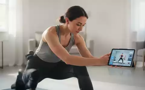 Eine Person dehnt sich in einer hellen Umgebung, im Hintergrund ein unscharfes Tablet mit einer Fitness-App. - Foto: über boerse-global.de