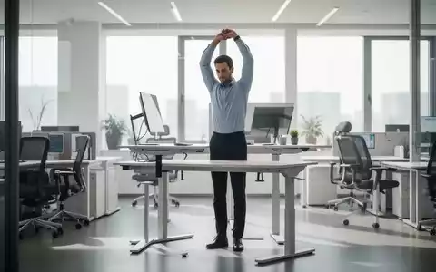 Ein Büroarbeiter steht an einem höhenverstellbaren Schreibtisch und dehnt sich, mit ergonomischen Möbeln im Hintergrund. - Foto: über boerse-global.de