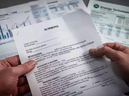 Eine Nahaufnahme einer Hand, die ein juristisches Dokument hält, mit verschwommenen Finanzdiagrammen im Hintergrund. - Foto: über boerse-global.de