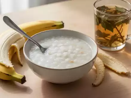 Eine Schale Reisbrei, eine geschälte Banane und ein Glas Kräutertee auf einem Holztisch, symbolisieren Schonkost bei Durchfall. - Foto: über boerse-global.de
