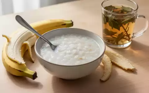 Eine Schale Reisbrei, eine geschälte Banane und ein Glas Kräutertee auf einem Holztisch, symbolisieren Schonkost bei Durchfall. - Foto: über boerse-global.de