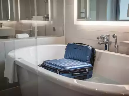 Ein offener Koffer steht in einer sauberen, gefliesten Badewanne in einem Hotelbad, symbolisiert Reisehygiene. - Foto: über boerse-global.de