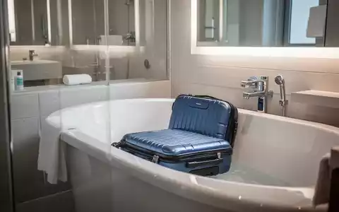 Ein offener Koffer steht in einer sauberen, gefliesten Badewanne in einem Hotelbad, symbolisiert Reisehygiene. - Foto: über boerse-global.de