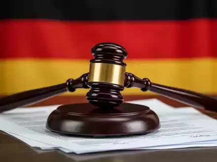Ein Richterhammer liegt auf juristischen Dokumenten, mit der leicht verschwommenen deutschen Flagge im Hintergrund. - Foto: über boerse-global.de