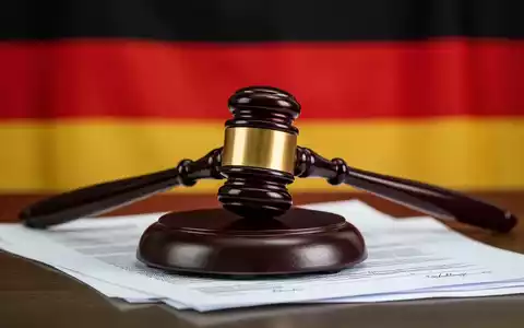 Ein Richterhammer liegt auf juristischen Dokumenten, mit der leicht verschwommenen deutschen Flagge im Hintergrund. - Foto: über boerse-global.de