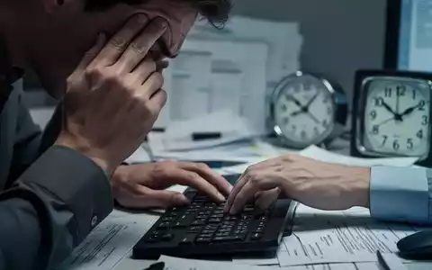 Nahaufnahme von Händen, eine Hand hält sich den Kopf vor Stress, die andere liegt auf einer Tastatur. Büroumgebung, späte Stunde. - Foto: über boerse-global.de