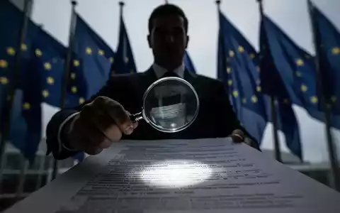 Eine schattenhafte Figur in einem Anzug untersucht ein juristisches Dokument mit einer Lupe vor EU-Flaggen. - Foto: über boerse-global.de