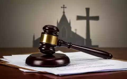 Ein Richterhammer liegt auf juristischen Dokumenten, mit einer angedeuteten Kirchen- oder Kreuzsilhouette im Hintergrund. - Foto: über boerse-global.de