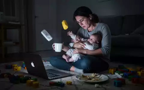 Eine erschöpfte Mutter arbeitet am Laptop, während sie ein Baby hält. Spielzeug und Geschirr liegen verstreut herum. - Foto: über boerse-global.de