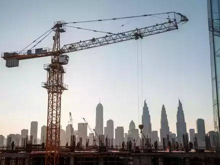 Ein riesiger Bau-Kran vor einem klaren Himmel mit einer Stadtsilhouette im Hintergrund, der moderne Hochbau symbolisiert. - Foto: über boerse-global.de
