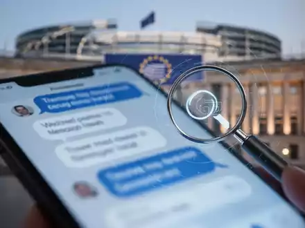 Smartphone-Bildschirm mit Chatblasen und Lupensymbol, Symbol für Chatkontroll-Gesetze. Europäisches Parlament unscharf im Hintergrund. - Foto: über boerse-global.de