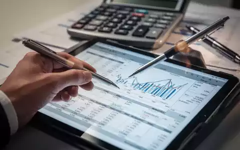 Hand hält Stift, zeigt auf Finanztabelle auf Tablet, mit Taschenrechner und Stift im Hintergrund. - Foto: über boerse-global.de